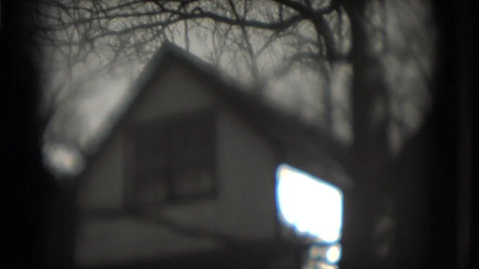 1975 Washington, DC 8mm frame showing a soft-focus gabled house partly obscured by bare branches and dark film edges.