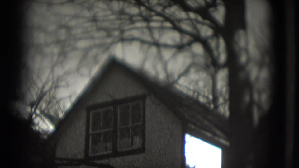 1975 Washington, DC 8mm frame of a soft-focus gabled house under bare branches, with bright sky visible near the right edge.