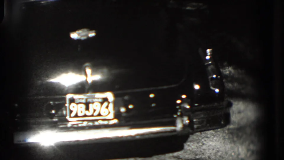 1975 Washington, DC home-movie frame showing the rear of a dark classic car with plate 9BJ96 and a reflective chrome bumper.