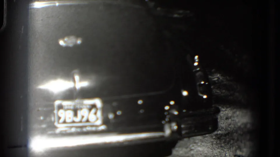Soft 8mm frame of the same Washington, DC car rear with plate 9BJ96, chrome bumper glare and dark roadside background.