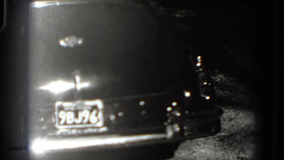 Blurred black-and-white 8mm view of a dark classic car rear in the documented 1975 Washington, DC footage.