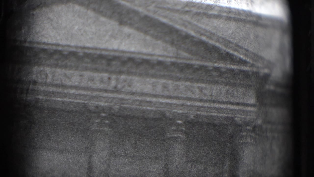 Soft black-and-white view of a classical building facade with columns and a pediment.