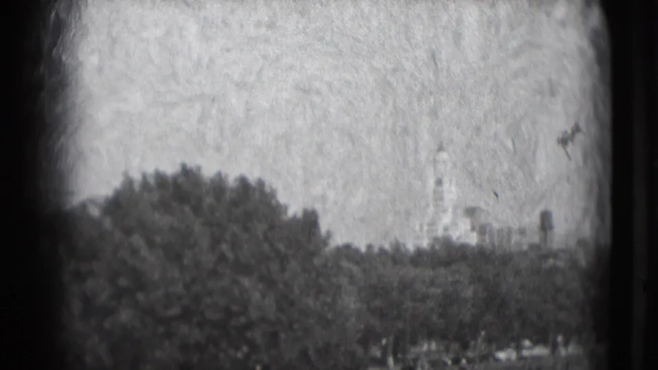 Grainy 1975 Washington, DC home-movie frame with trees in the foreground and a distant monument-like structure in soft focus.