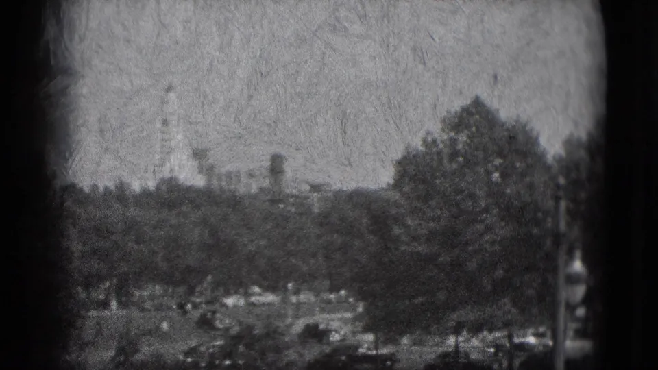 Grainy Washington, DC home-movie frame showing a tree-lined public landscape with small light shapes and a distant monument-like feature.