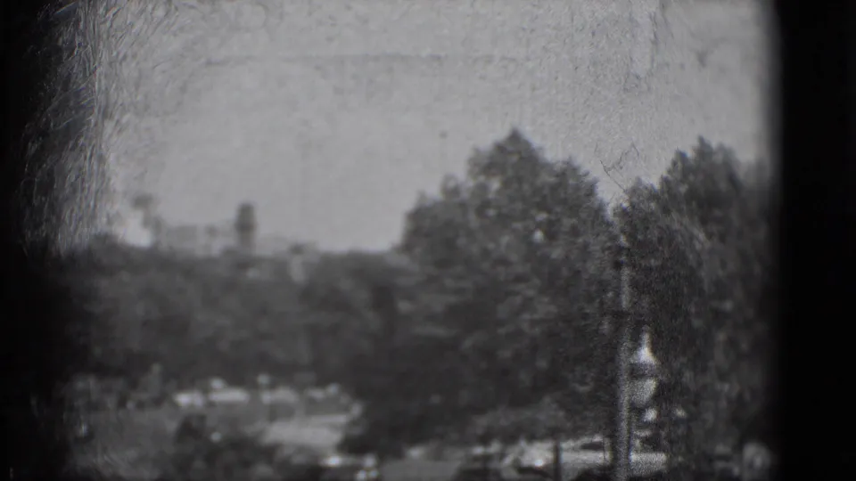 1975 8mm view in Washington, DC with treetops, faint traffic, and a dark window frame partially blocking the scene.