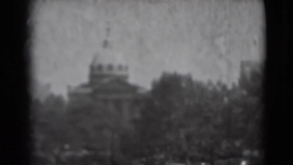 Soft 1975 Washington, DC home-movie frame with the U.S. Capitol dome centered behind trees and window framing.