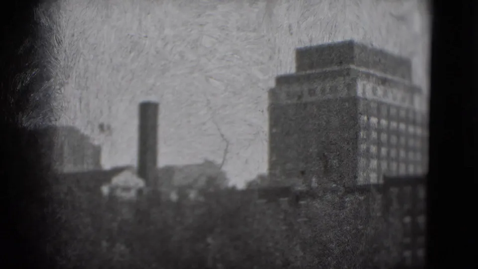 1975 Washington, DC frame showing a tall rectangular building, chimney, tree canopy, haze, and dark 8mm frame borders.