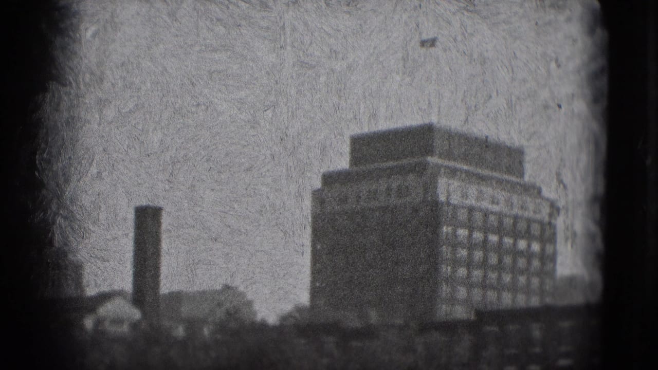 1975 Washington DC home-movie frame showing a hazy tall building with rows of windows, a nearby chimney, rooftops, and heavy 8mm grain.