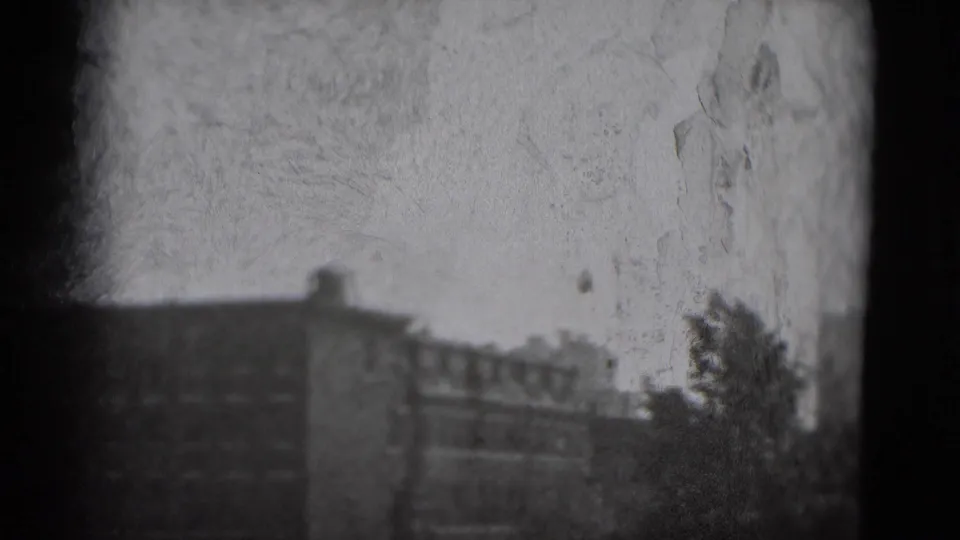 1975 Washington DC skyline frame showing lower buildings, rooftop lines, a dark tree shape, and pronounced scratches in the 8mm film image.