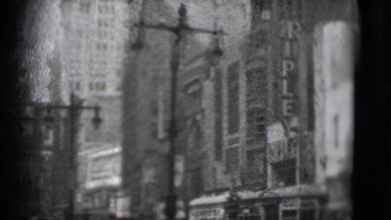 Soft black-and-white view of tall city buildings, streetlamps, and a commercial street edge.