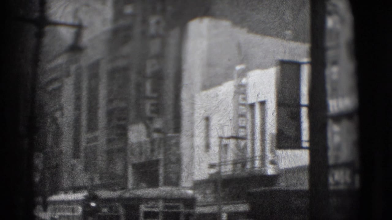 Blurred city street view with building fronts, vertical signage, and a bright marquee-like facade.