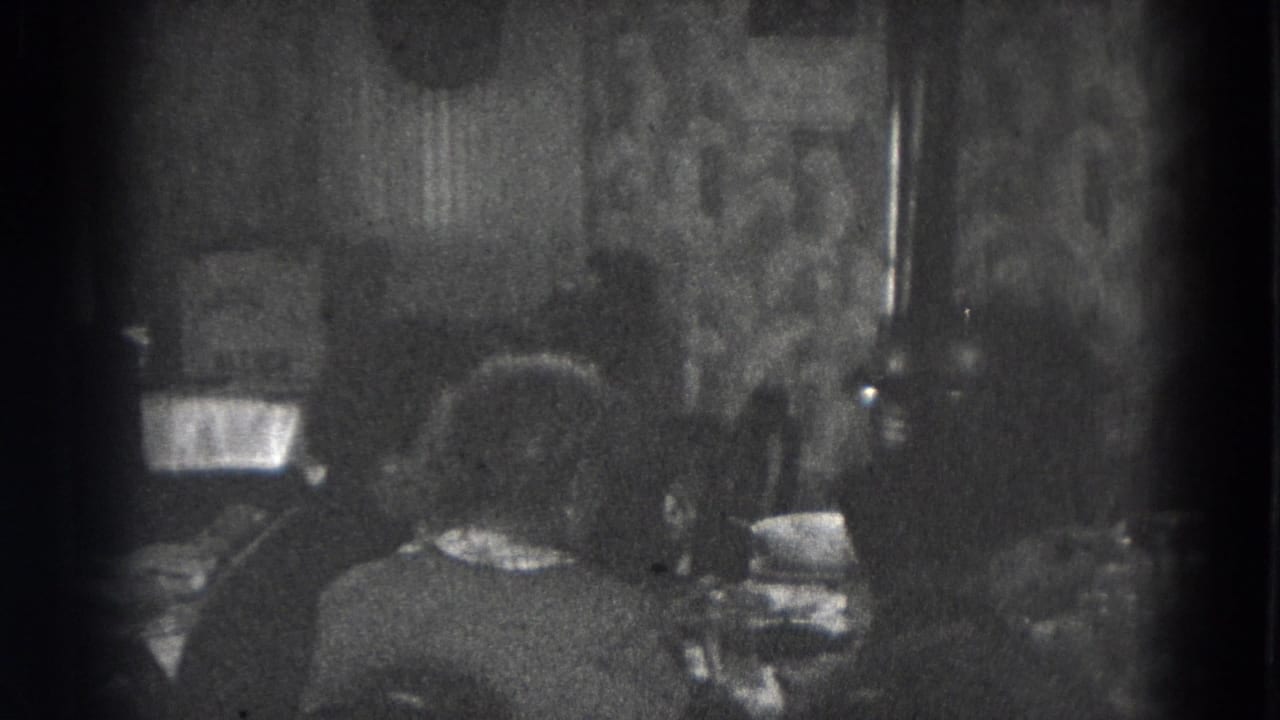 Two adults are viewed from behind at a dining table in a patterned domestic interior, consistent with the Lincoln home-movie metadata.