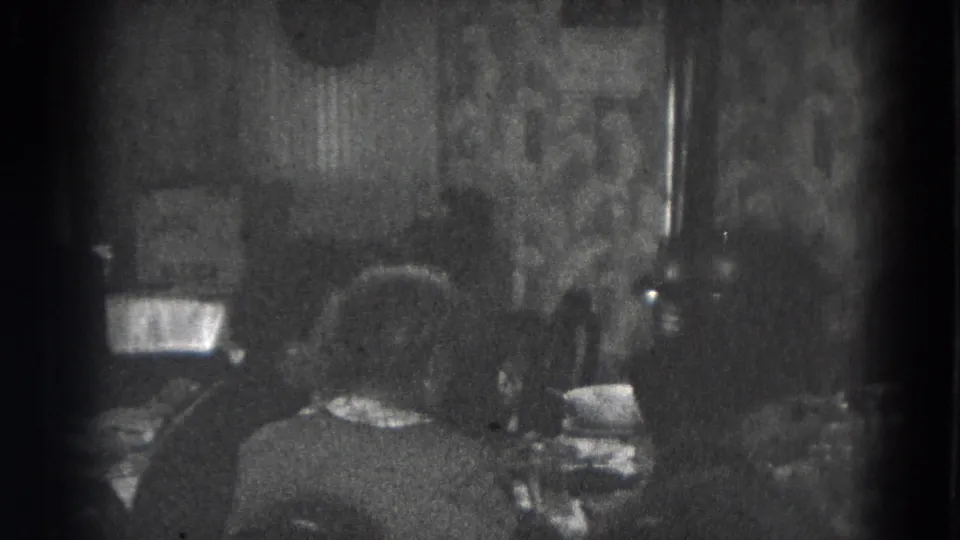 Two adults are viewed from behind at a dining table in a patterned domestic interior, consistent with the Lincoln home-movie metadata.