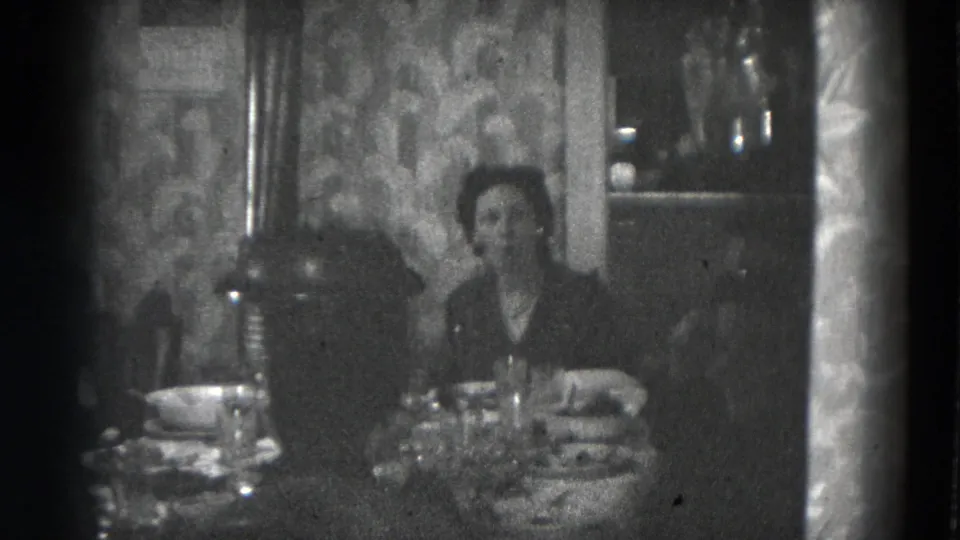 A woman sits at the dining table in the Lincoln home-movie footage, with tableware, food dishes, and patterned wallpaper visible.