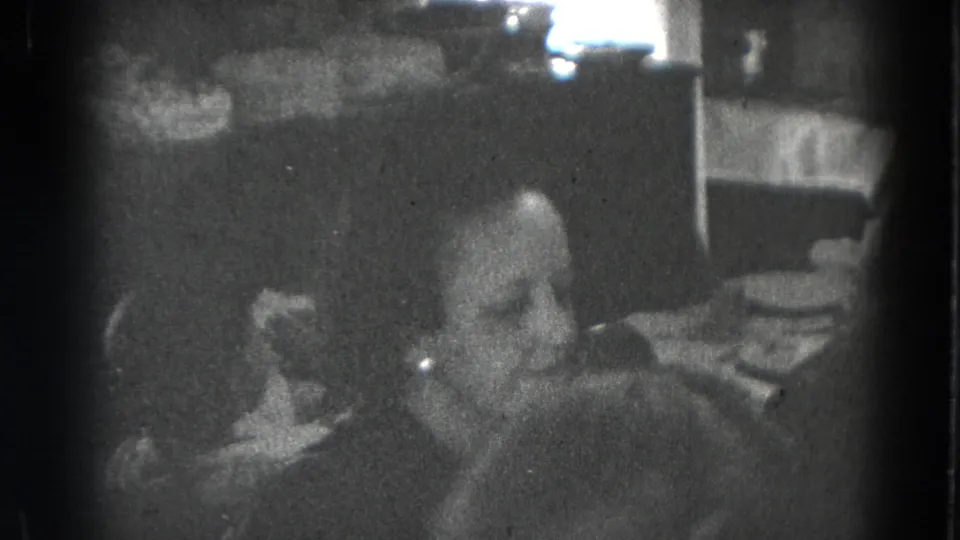 A seated woman is seen in close view near a set table in black-and-white 8mm footage from Lincoln, Nebraska.