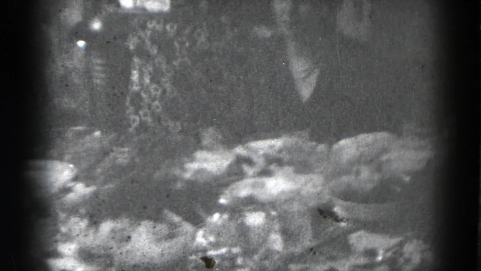 Grainy 8mm frame of a person standing by a crowded dining table with plates, bowls, and serving items.