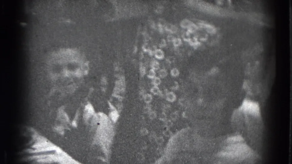 Grainy Lincoln, Nebraska home-movie frame with two visible faces near a decorated dessert or cake on a crowded party table.