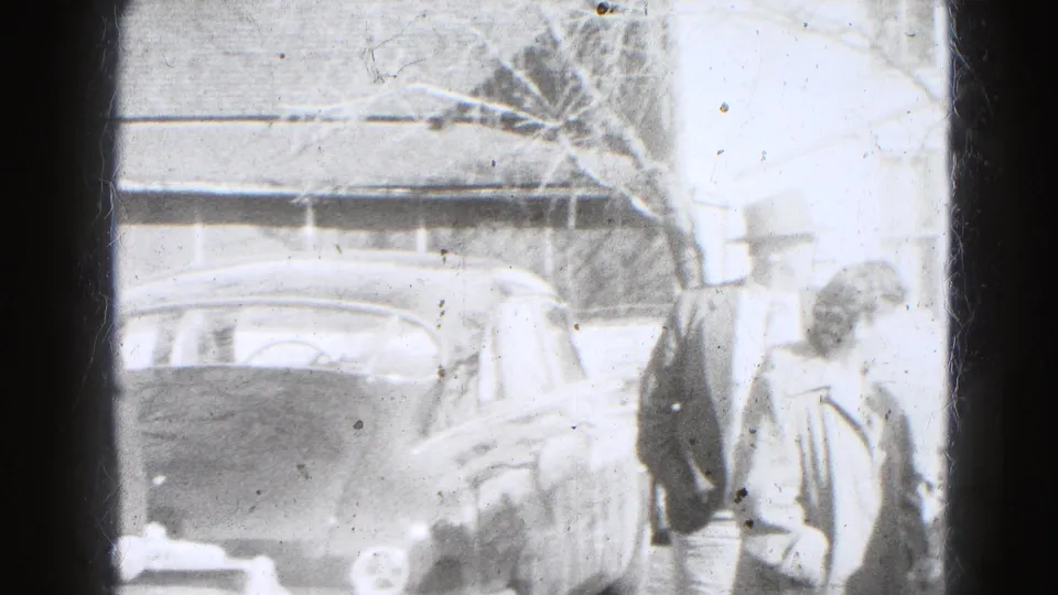 In Lincoln, Nebraska home-movie footage from 1947, adults in coats stand near a parked car outside a residential house.