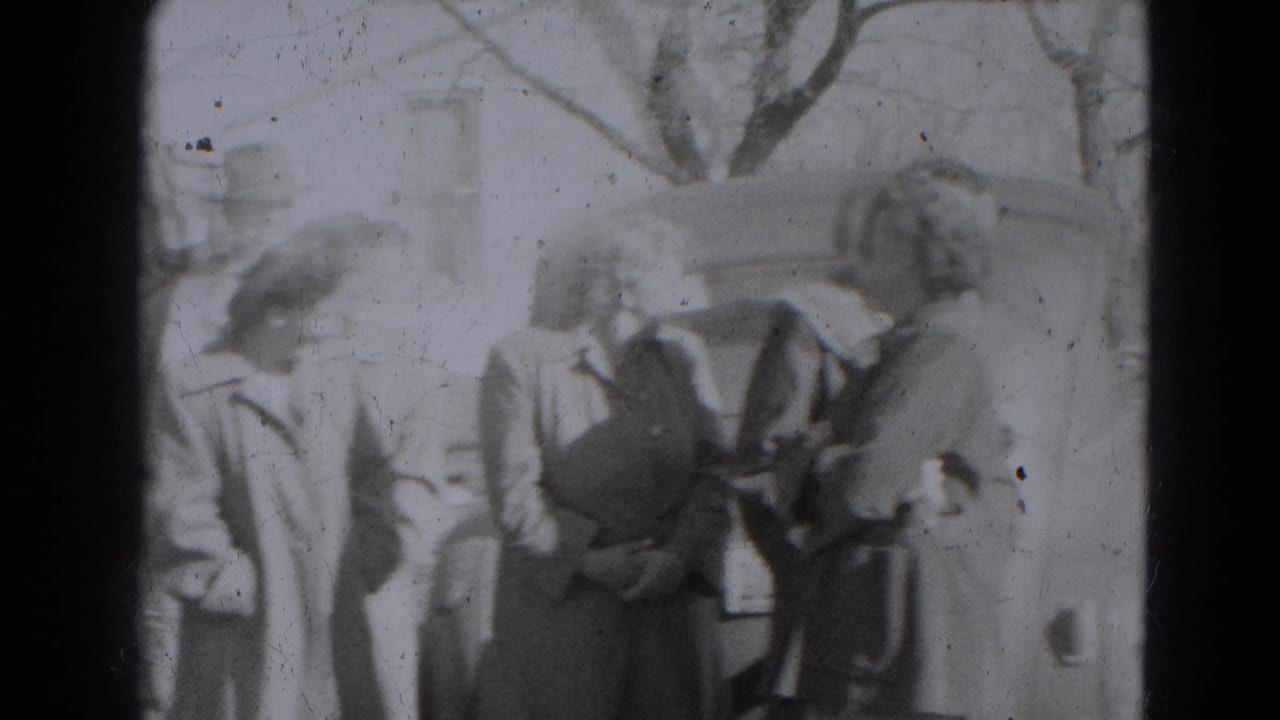 A group of adults in coats and hats stands outdoors near a residential house in the supplied 1947 Lincoln, Nebraska clip.