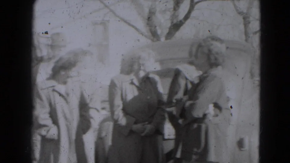 A group of adults in coats and hats stands outdoors near a residential house in the supplied 1947 Lincoln, Nebraska clip.