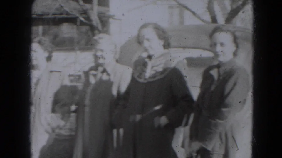 Two women in coats and head coverings face the camera near a parked car during the Lincoln, Nebraska home-movie scene.