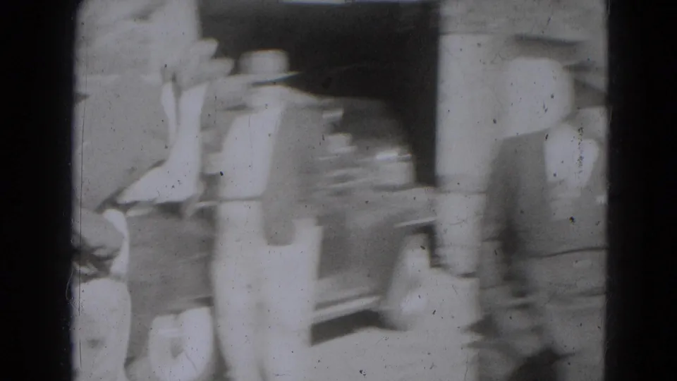 A blurred adult moves past the camera beside the car and building in the Lincoln, Nebraska home-movie footage.