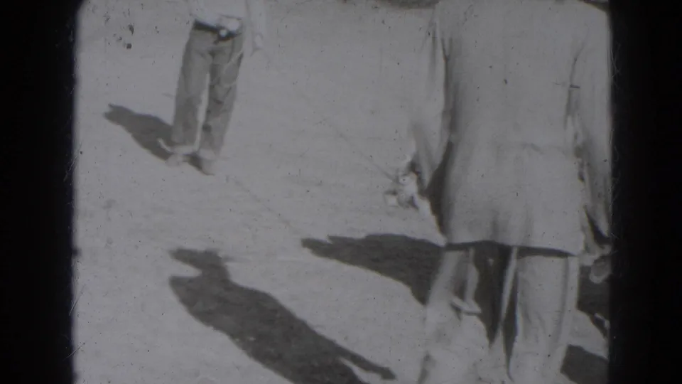 1940s 8mm home-movie frame from Lincoln, Nebraska, showing cropped adults outdoors in bright sun with long shadows on the ground.