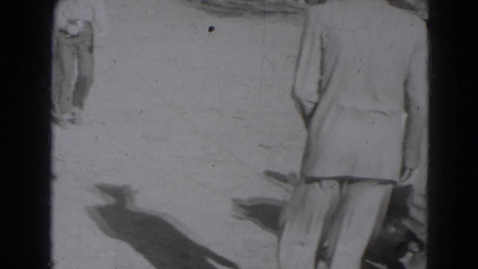 1940s Lincoln home-movie frame with two cropped adults in light clothing on sunlit outdoor ground, bordered by the 8mm frame edge.