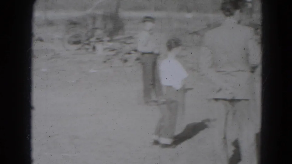 Men and boys in hats and light shirts stand in a rural dirt yard, watching the animal activity nearby in 1940s Nebraska home-movie footage.