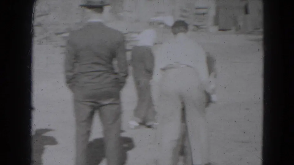 Several people face away from the camera in a dirt yard while a young cow moves near buildings in Lincoln, Nebraska.
