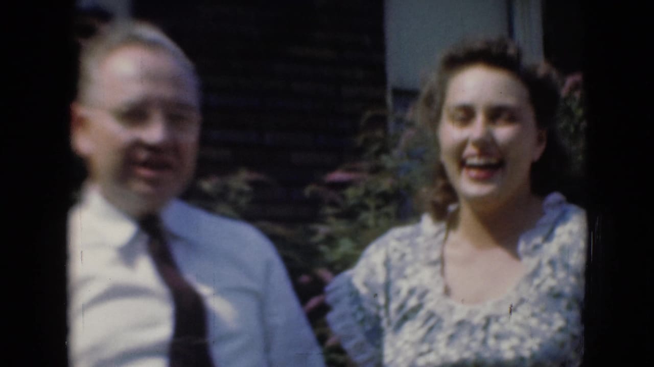 Smiling man in shirt and tie beside a woman in a patterned dress outdoors.