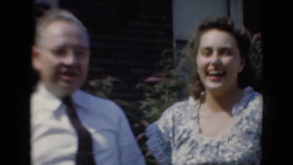 In archival home-movie footage from Middletown, Pennsylvania, two adults smile toward the camera in a sunlit garden setting.