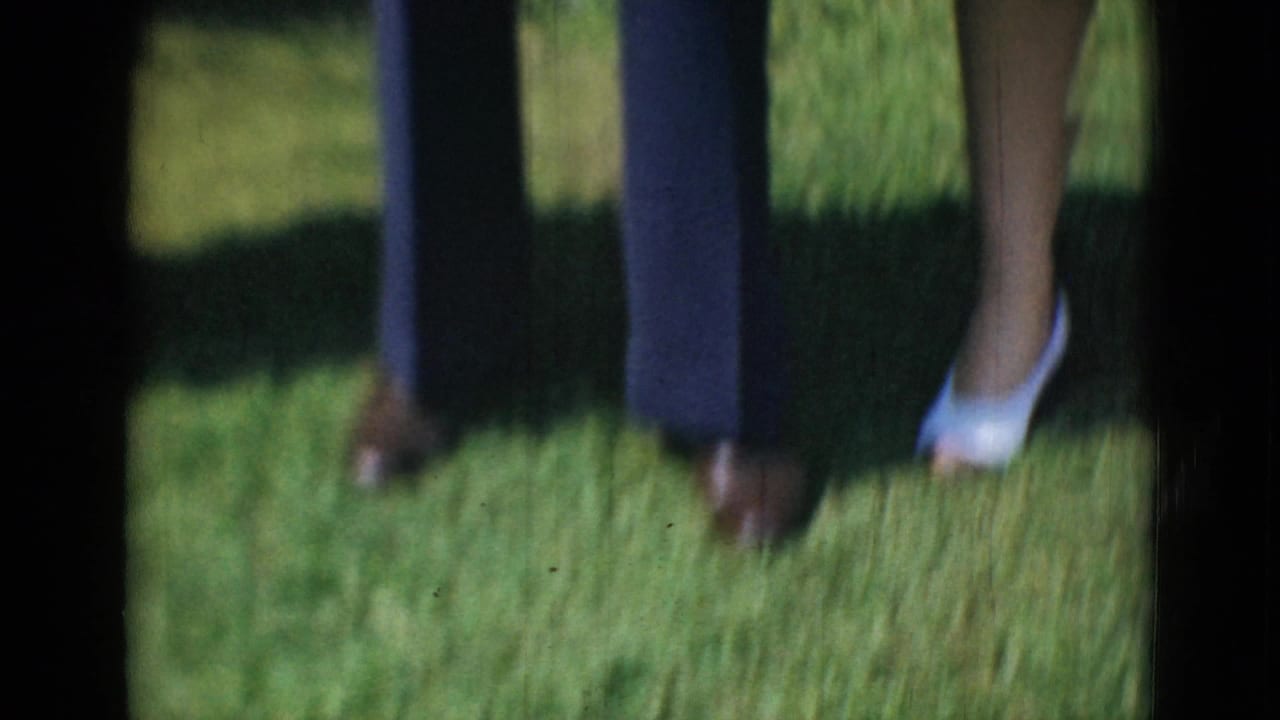 A cropped home-movie frame shows adults' lower legs and shoes on grass, likely part of the same outdoor family scene.