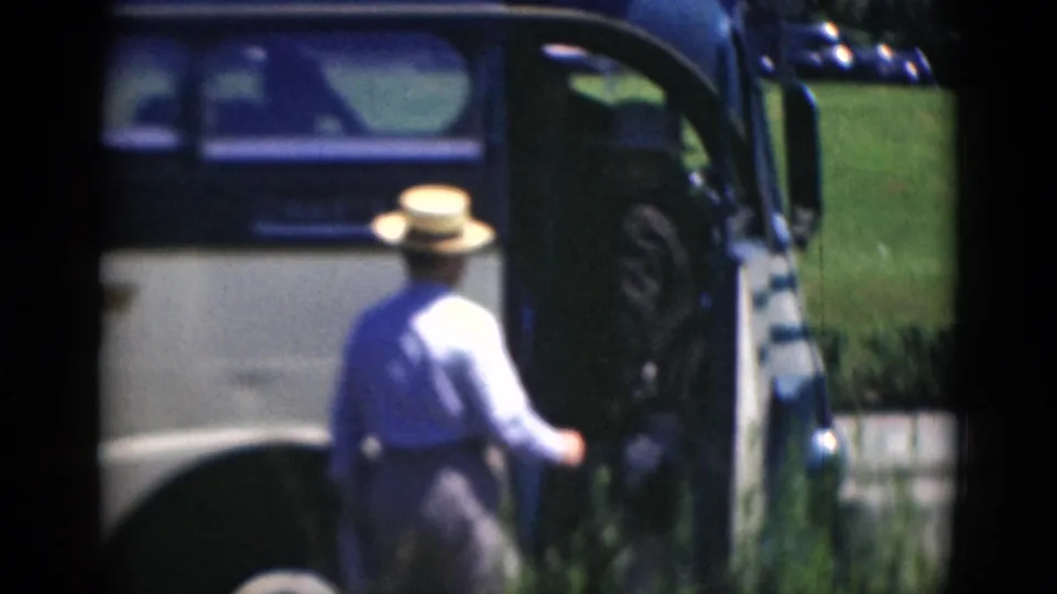 In cataloged 1940s Middletown footage, an adult man in a straw hat stands near the side door of a stopped bus.