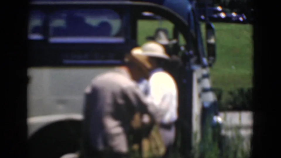 Two adult men in hats stand beside the stopped bus, partly obscured by soft focus and close framing.