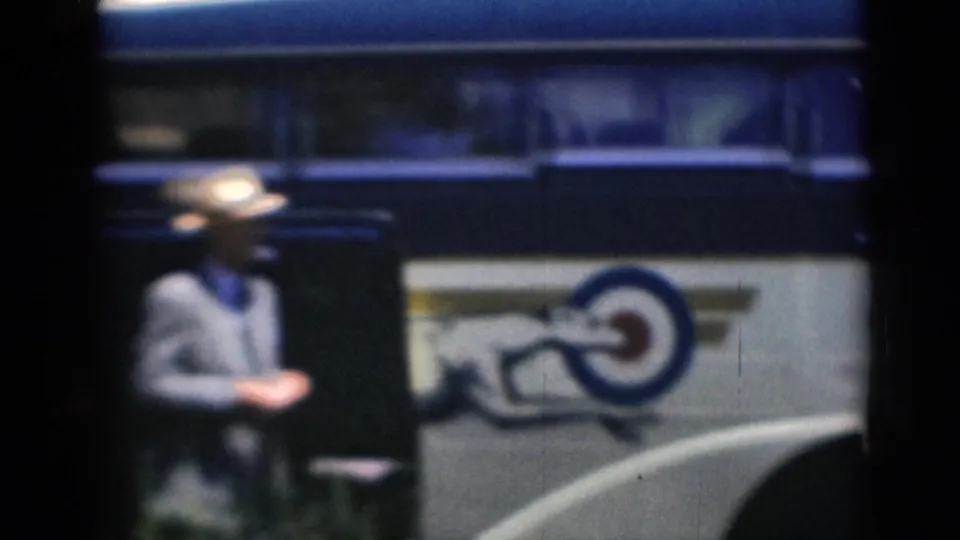 A man walks past the side of the bus, where a running-dog style emblem is visible on the painted panel.