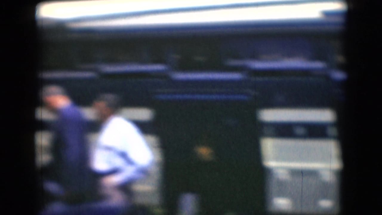 Soft-focus view of men near a blue-and-white bus with dark film borders.