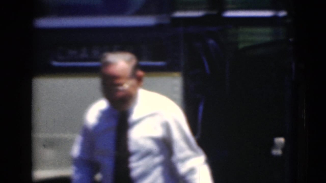 A man in a light shirt and dark tie stands beside the antique bus, rendered with motion blur and deep shadow.