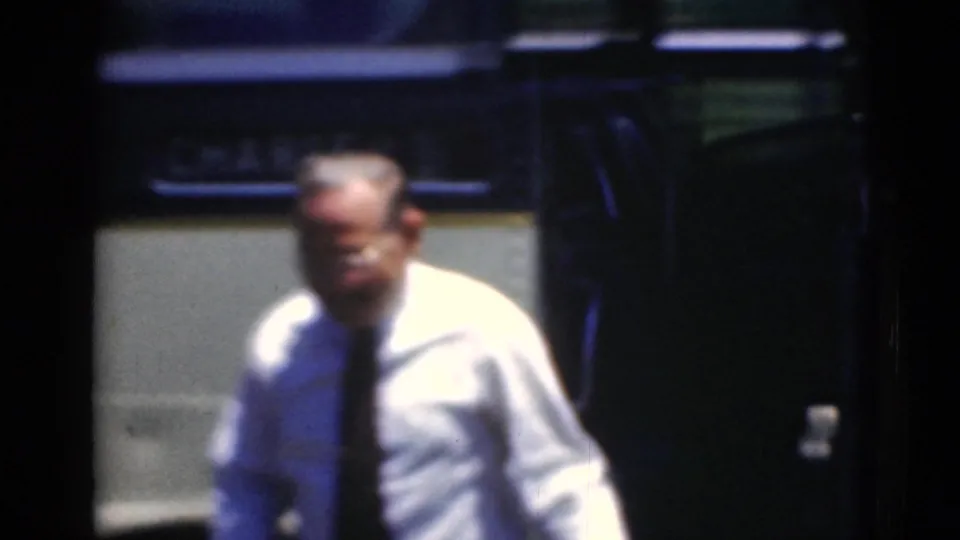 A man in a light shirt and dark tie stands beside the antique bus, rendered with motion blur and deep shadow.