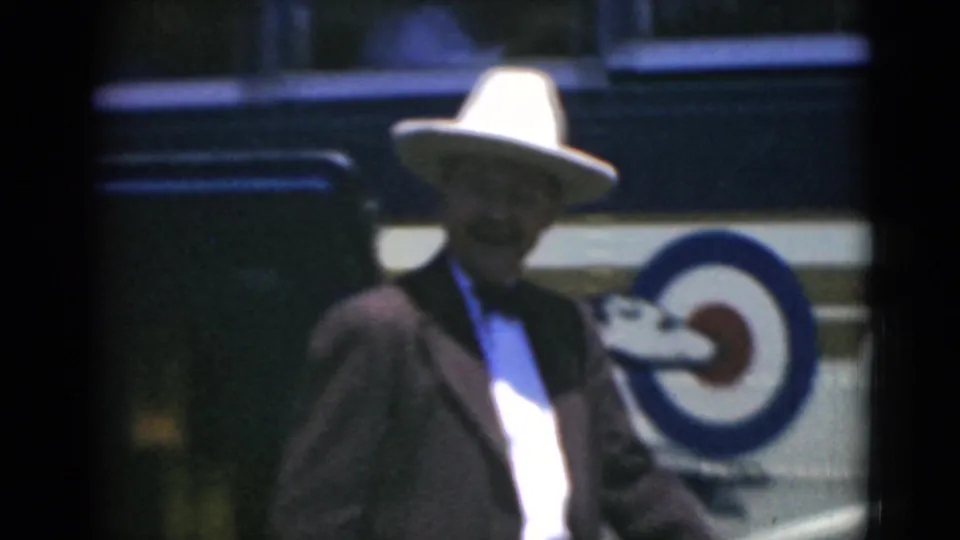 A second man wearing a white brimmed hat and dark suit stands near the antique bus in Middletown, Pennsylvania.