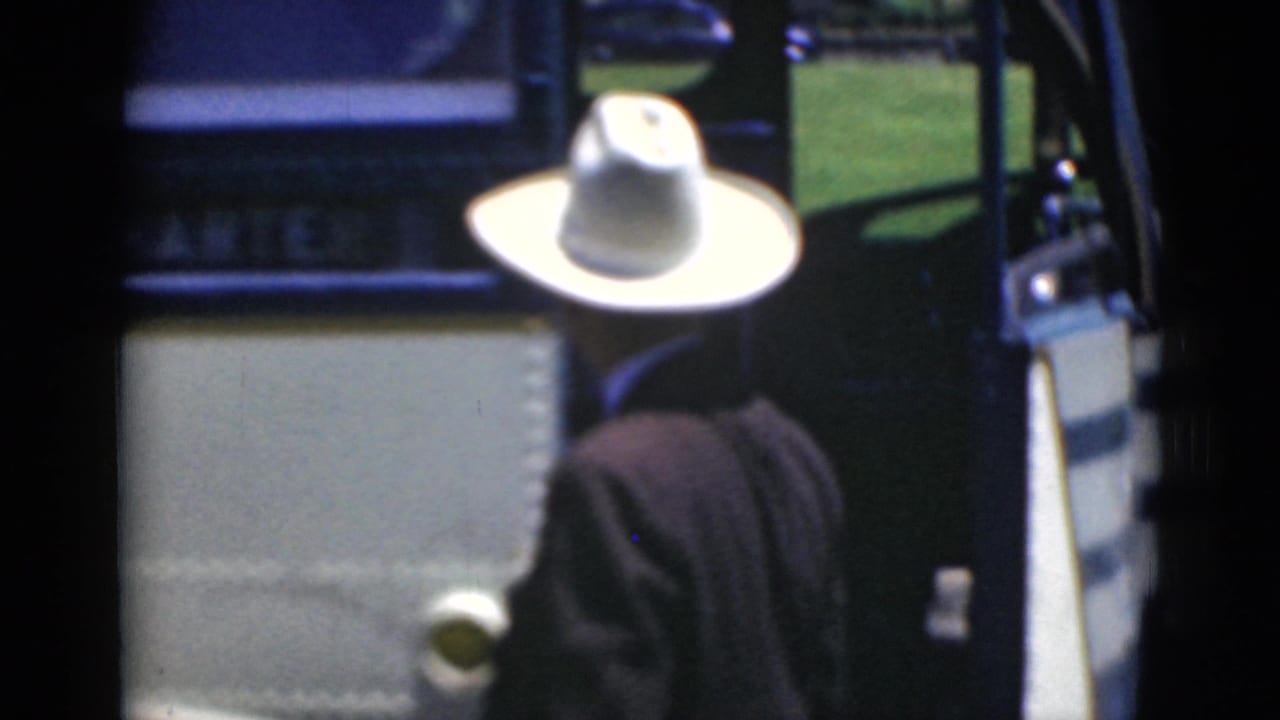 Man in a white cowboy hat walking away from a bus doorway.