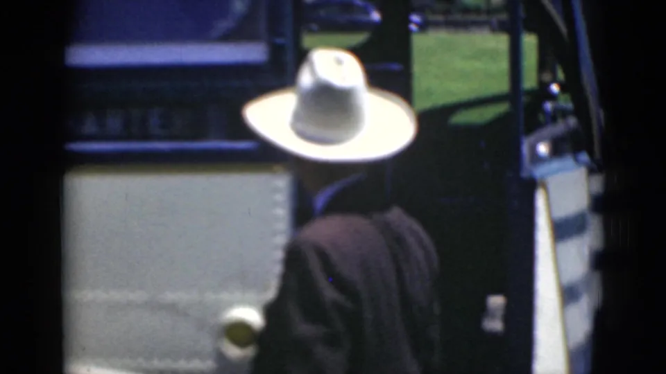 A man in a light cowboy-style hat moves beside the bus door, with grass visible beyond the vehicle.
