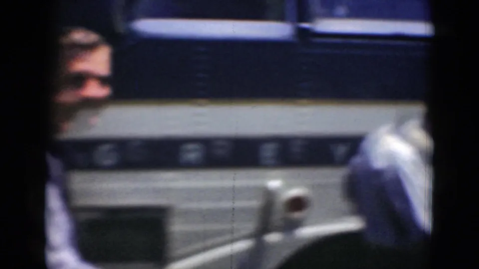 The bus fills most of the frame as a man in a light shirt is partly hidden by the vehicle and another figure at the edge.