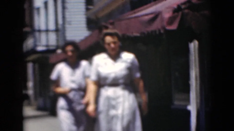 Two women in light dresses walk toward the camera on a Middletown sidewalk, with a red awning and building fronts behind them.