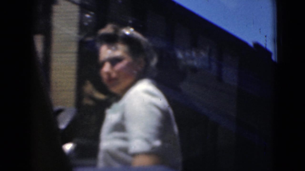 A woman in a light short-sleeved dress turns toward the camera on a Middletown street, with a dark car and storefront awning behind her.
