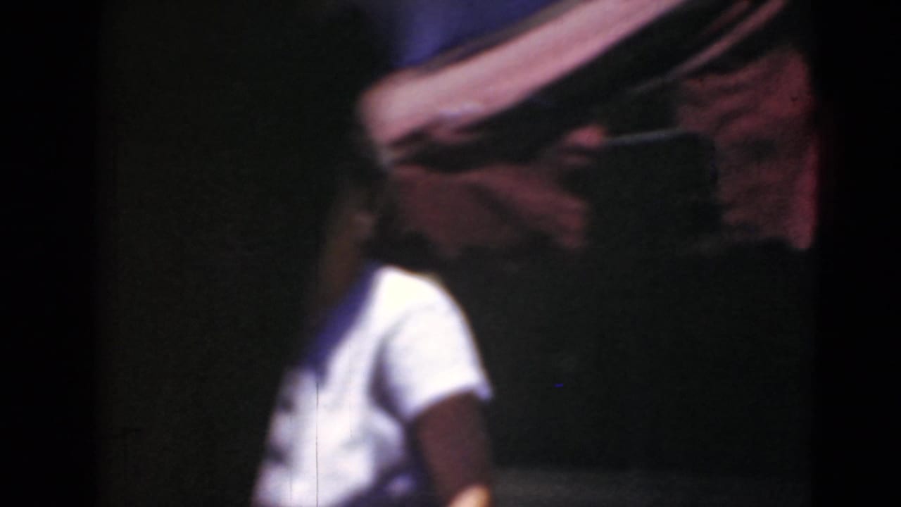 Woman in a white shirt partly obscured beside a dark car and red awning.