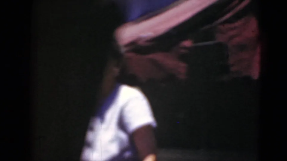 In Middletown, Pennsylvania home-movie footage, a woman in a white shirt is partly framed near a dark car and a red awning.