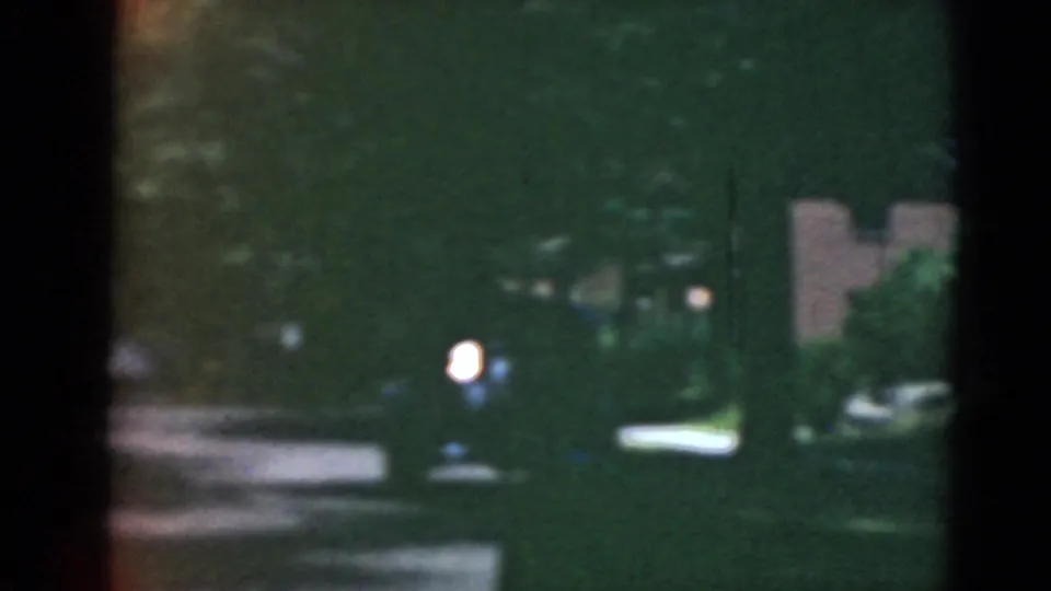 A darker 8mm street view shows trees, houses, parked cars, and a bright light or reflection in the distance.