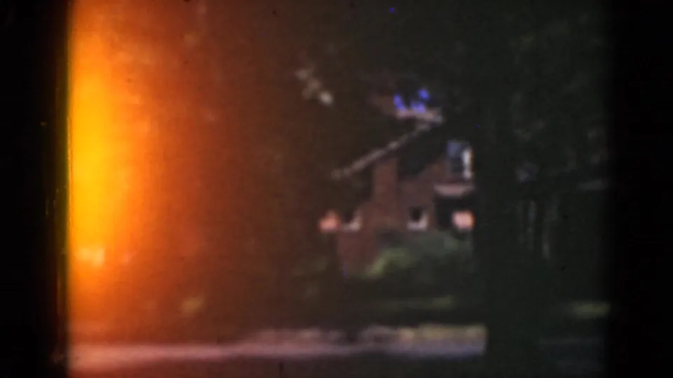 A residential house and lawn appear behind orange light flare and dark film borders, with trees filling much of the frame.