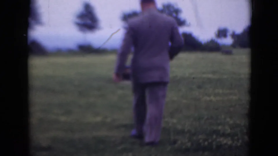 A rear view shows the suited man farther from the camera in the open field, with visible grain, color shift, and dark frame borders.